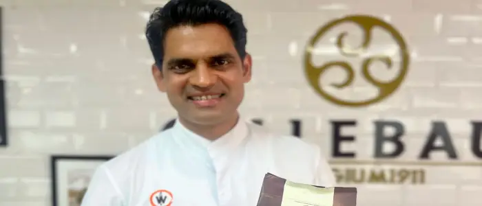 Smiling director of the academy in a chef coat proudly holding a award, standing in front of the Callebaut logo wall.
